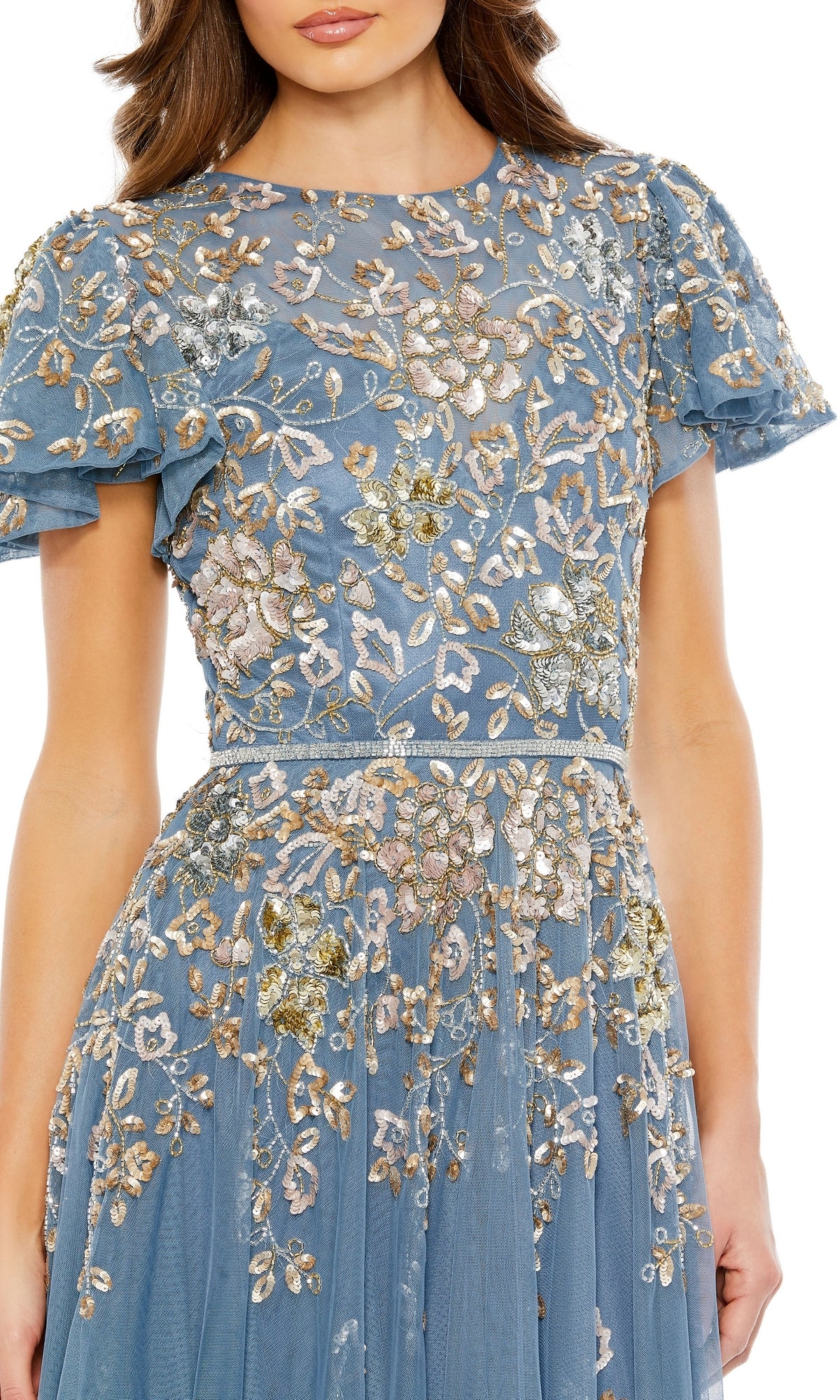 A woman is seen from the head to upper body wearing the Mac Duggal 5717, a short sleeve beaded formal dress in blue with sheer fabric and elaborate gold, white, and silver floral embroidery.